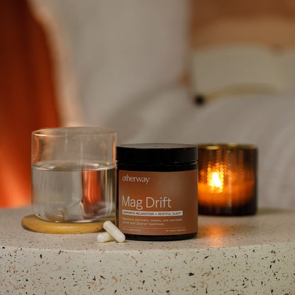 Jar labeled 'Mag Drift' and a glass of water on a stone surface with a warm background.